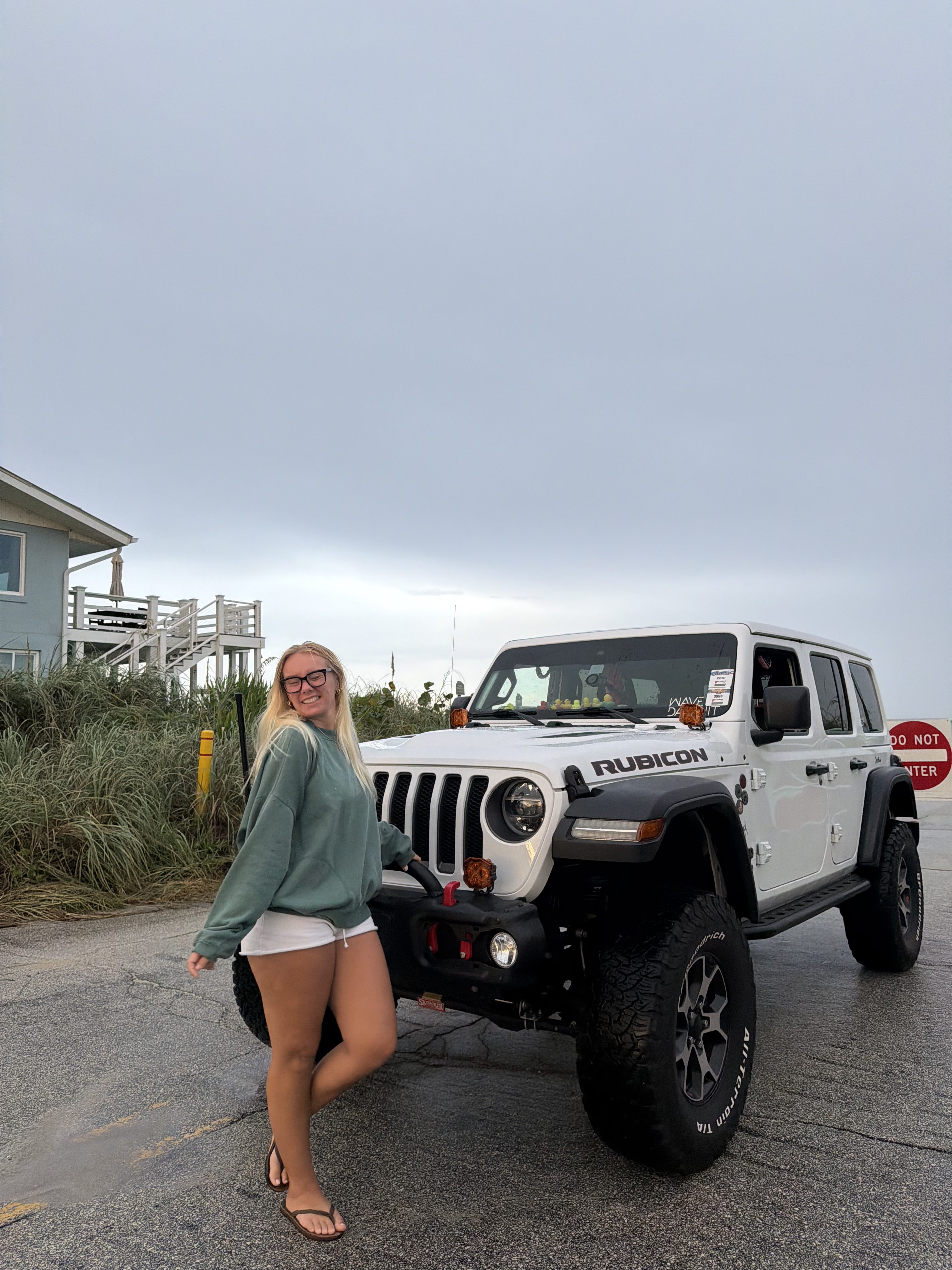 Blondie standing with her white Jeep Wrangler Rubicon at the beach